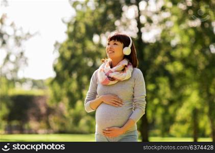 pregnancy, people and technology concept - happy pregnant asian woman in headphones at park listening to music. happy pregnant asian woman in headphones at park