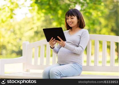 pregnancy, people and technology concept - happy pregnant asian woman with tablet pc computer sitting on park bench. happy pregnant asian woman with tablet pc at park