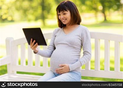 pregnancy, people and technology concept - happy pregnant asian woman with tablet pc computer sitting on park bench. happy pregnant asian woman with tablet pc at park