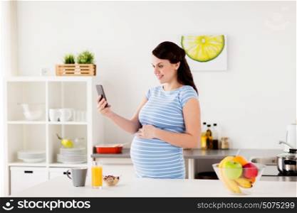 pregnancy, people and technology concept - happy pregnant woman with smartphone taking selfie and having breakfast at home kitchen. happy pregnant woman with smartphone at kitchen