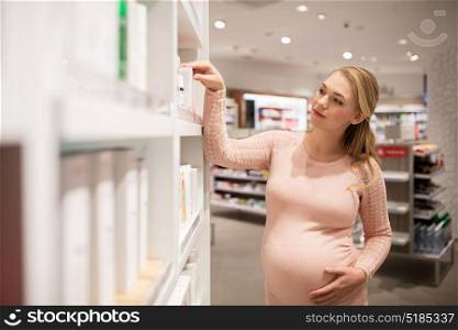 pregnancy, people, healthcare, beauty and bodycare concept - pregnant woman choosing medicine at pharmacy or cosmetics store. pregnant woman at pharmacy or cosmetics store