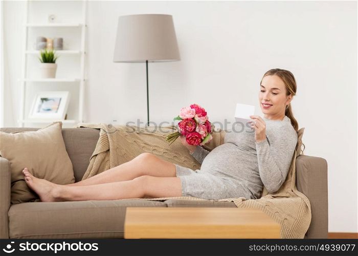 pregnancy, people, holidays and expectation concept - happy pregnant woman with flowers and greeting card at home. happy pregnant woman with flowers and card at home