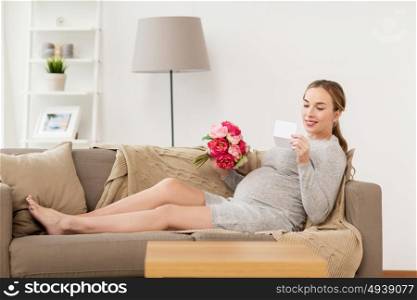 pregnancy, people, holidays and expectation concept - happy pregnant woman with flowers and greeting card at home. happy pregnant woman with flowers and card at home