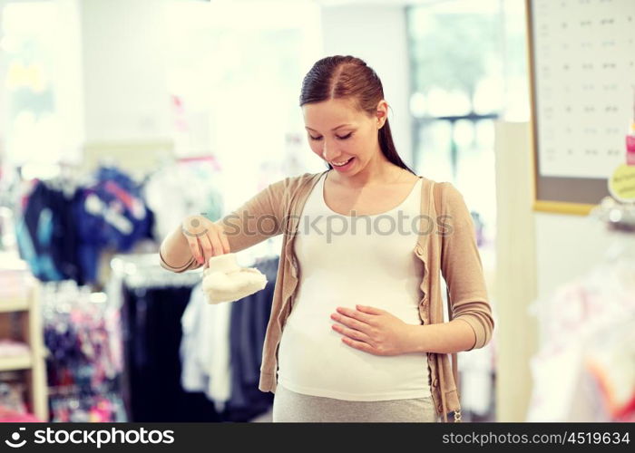 pregnancy, people, sale and expectation concept - happy pregnant woman shopping and buying baby baby bootees at children clothing store