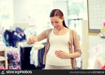 pregnancy, people, sale and expectation concept - happy pregnant woman shopping and buying baby baby bootees at children clothing store