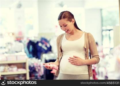 pregnancy, people, sale and expectation concept - happy pregnant woman shopping and buying baby socks at children clothing store