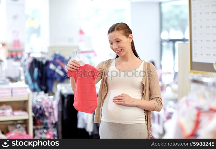 pregnancy, people, sale and expectation concept - happy pregnant woman shopping and buying baby bodysuit at children clothing store