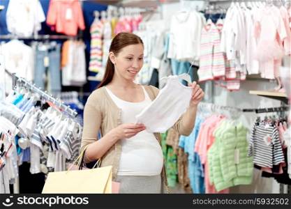 pregnancy, people, sale and expectation concept - happy pregnant woman with shopping bag buying baby bodysuit at children clothing store