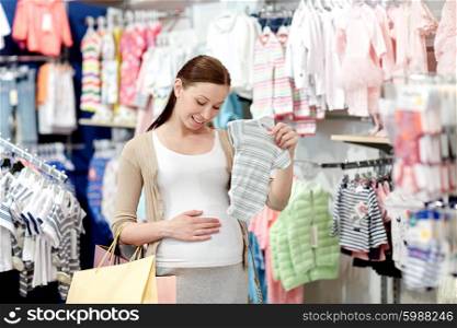 pregnancy, people, sale and expectation concept - happy pregnant woman with shopping bag buying baby bodysuit at children clothing store
