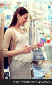 pregnancy, people, shopping, sale and expectation concept - happy pregnant woman choosing baby bottle at childrens store