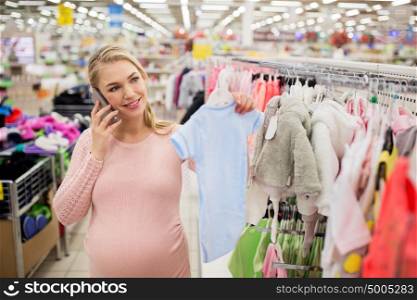 pregnancy, people, technology and shopping concept - happy pregnant woman with blue baby bodysuit calling on smartphone at clothing store. pregnant woman with baby clothes at clothing store