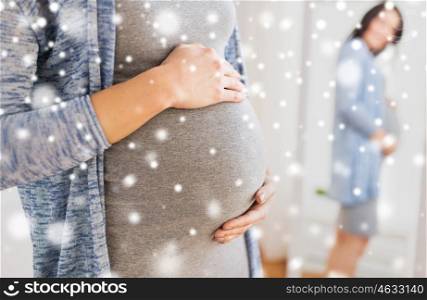 pregnancy, people, winter, christmas and expectation concept - close up of happy pregnant woman with big belly looking to mirror at home over snow
