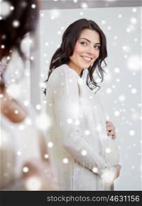 pregnancy, people, winter, christmas and expectation concept - happy pregnant woman looking to mirror at home over snow