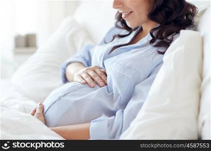 pregnancy, rest, people and expectation concept - close up of happy smiling pregnant woman lying in bed and touching her belly at home