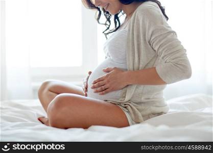 pregnancy, rest, people and expectation concept - close up of happy smiling pregnant woman sitting in bed and touching her belly at home