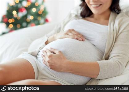 pregnancy, rest, people and expectation concept - close up of happy smiling pregnant woman lying in bed and touching her belly over christmas tree background