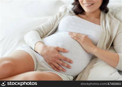 pregnancy, rest, people and expectation concept - close up of happy smiling pregnant woman lying in bed and touching her belly at home