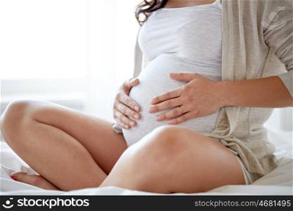 pregnancy, rest, people and expectation concept - close up of pregnant woman sitting in bed and touching her belly at home