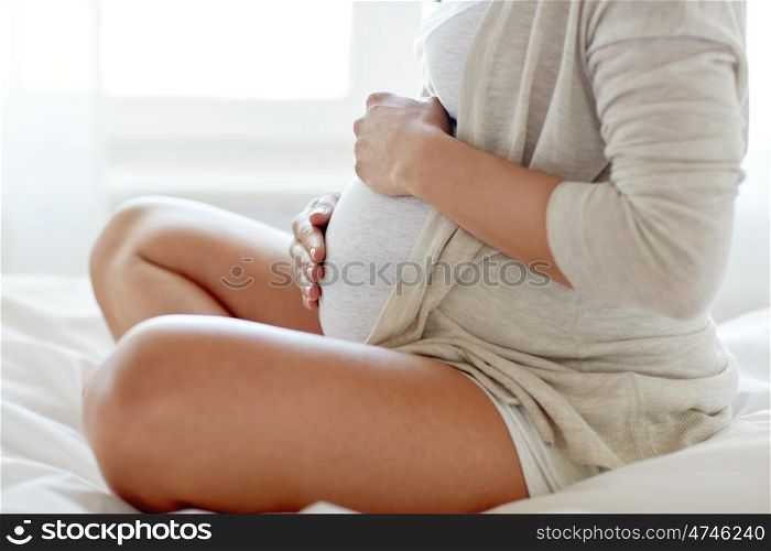 pregnancy, rest, people and expectation concept - close up of pregnant woman sitting in bed and touching her belly at home