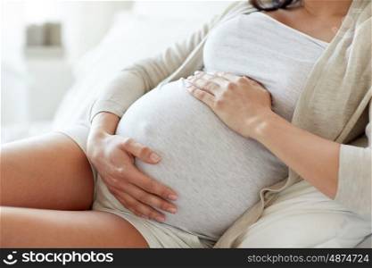 pregnancy, rest, people and expectation concept - close up of pregnant woman lying in bed and touching her belly at home