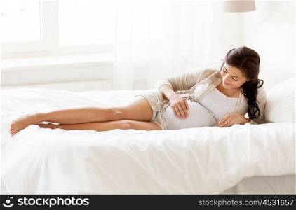 pregnancy, rest, people and expectation concept - happy pregnant woman lying in bed and touching her belly at home bedroom