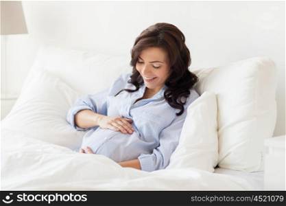 pregnancy, rest, people and expectation concept - happy pregnant woman lying on bed and touching her belly at home