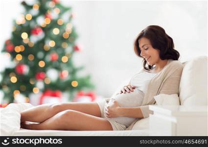pregnancy, rest, people and expectation concept - happy pregnant woman lying on bed and touching her belly over christmas tree background