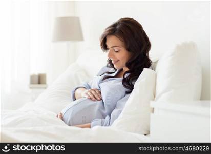 pregnancy, rest, people and expectation concept - happy pregnant woman lying on bed and touching her belly at home