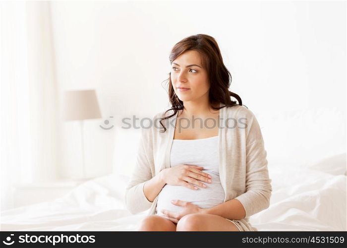 pregnancy, rest, people and expectation concept - happy pregnant woman sitting on bed and touching her belly at home. happy pregnant woman sitting on bed at home