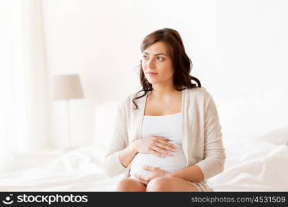 pregnancy, rest, people and expectation concept - happy pregnant woman sitting on bed and touching her belly at home. happy pregnant woman sitting on bed at home