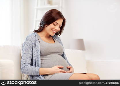 pregnancy, rest, people and expectation concept - happy pregnant woman sitting on sofa at home