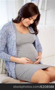pregnancy, rest, people and expectation concept - happy pregnant woman sitting on sofa at home