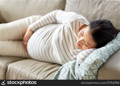 pregnancy, rest, people and expectation concept - happy smiling pregnant asian woman sleeping on sofa at home. pregnant asian woman sleeping on sofa at home