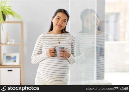 pregnancy, rest, people and expectation concept - happy smiling pregnant asian woman with mug drinking tea at home. happy pregnant woman drinking tea at home