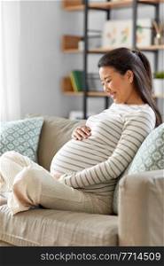 pregnancy, rest, people and expectation concept - happy smiling pregnant asian woman sitting on sofa at home. happy pregnant asian woman sitting on sofa at home