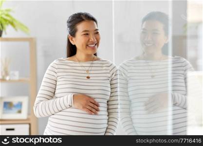 pregnancy, rest, people and expectation concept - happy smiling pregnant asian woman touching her belly at home. happy pregnant asian woman at home