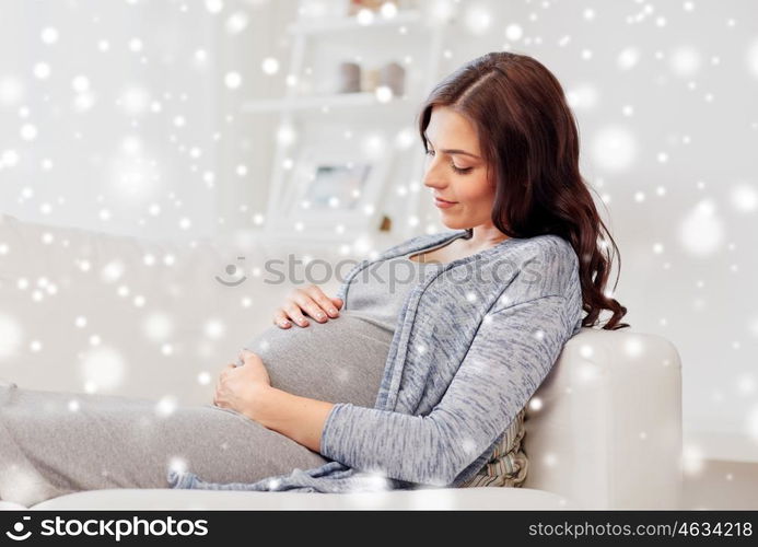 pregnancy, rest, people, winter and expectation concept - happy pregnant woman lying on sofa at home over snow