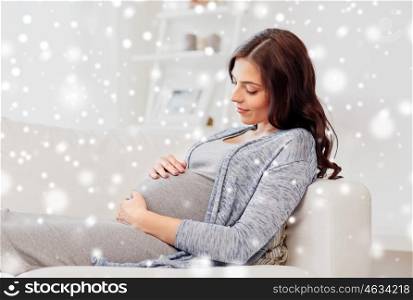 pregnancy, rest, people, winter and expectation concept - happy pregnant woman lying on sofa at home over snow