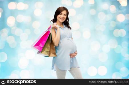 pregnancy, sale, motherhood, people and expectation concept - happy pregnant woman with shopping bags touching her big belly over blue holidays lights background