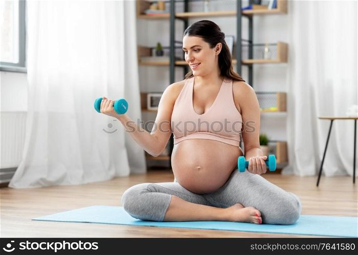 pregnancy, sport and fitness concept - happy pregnant woman with light dumbbells exercising at home. pregnant woman with dumbbells doing sports at home