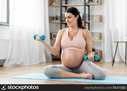 pregnancy, sport and fitness concept - happy pregnant woman with light dumbbells exercising at home. pregnant woman with dumbbells doing sports at home