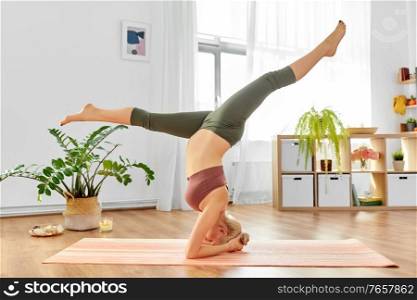 pregnancy, sport and people concept - happy pregnant woman doing yoga headstand split at home. pregnant woman doing yoga headstand split at home