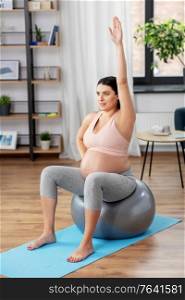 pregnancy, sport and people concept - happy pregnant woman exercising on fitness ball at home. pregnant woman exercising on fitness ball at home