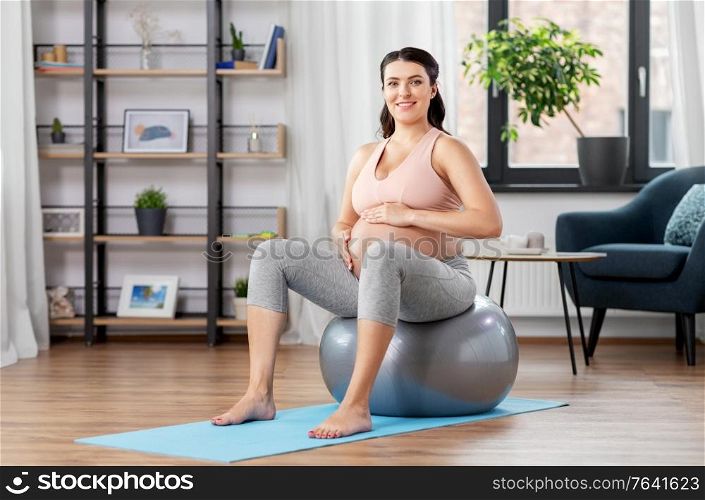pregnancy, sport and people concept - happy pregnant woman exercising on fitness ball at home. pregnant woman exercising on fitness ball at home