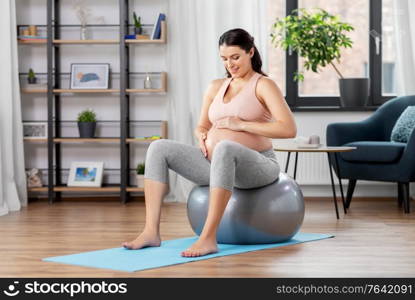 pregnancy, sport and people concept - happy pregnant woman exercising on fitness ball at home. pregnant woman exercising on fitness ball at home