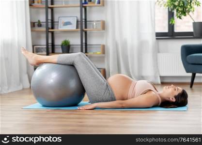 pregnancy, sport and people concept - happy pregnant woman exercising with fitness ball at home. pregnant woman training with fitness ball at home