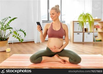 pregnancy, sport and people concept - happy pregnant woman with smartphone doing yoga at home. happy pregnant woman with phone doing yoga at home