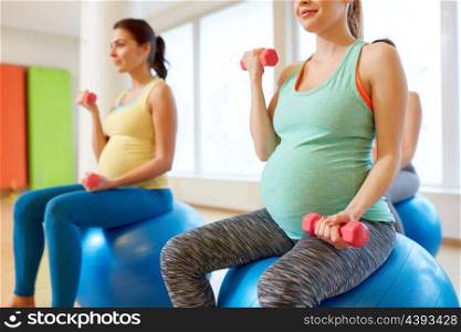 pregnancy, sport, fitness, people and healthy lifestyle concept - group of happy pregnant women with dumbbells on exercise ball in gym. pregnant women training with exercise balls in gym. pregnant women training with exercise balls in gym