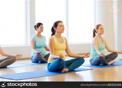 pregnancy, sport, fitness, people and healthy lifestyle concept - group of happy pregnant women exercising yoga and meditating in lotus pose in gym