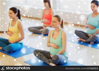 pregnancy, sport, fitness, people and healthy lifestyle concept - group of happy pregnant women exercising yoga and meditating in lotus pose in gym over snow
